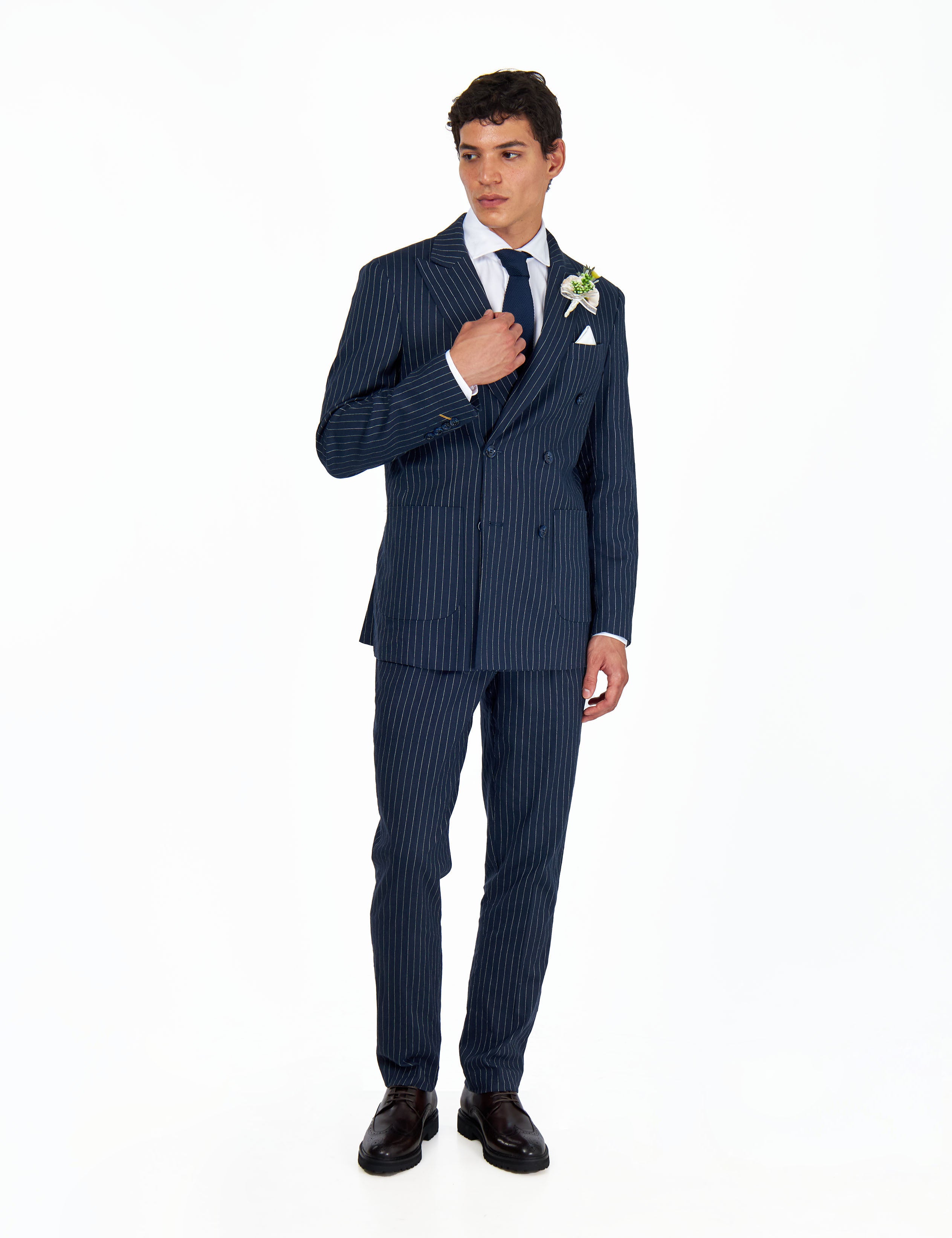 Man wearing a navy pinstripe suit with a white shirt and black shoes with white flower lapel pin